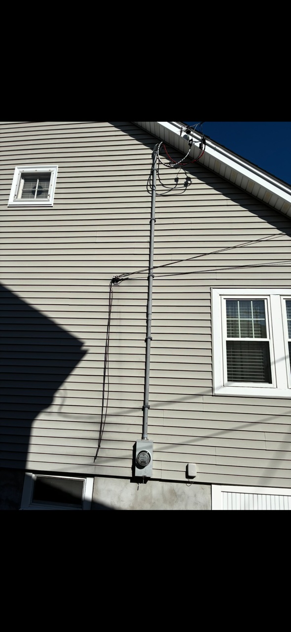 Boston Light & Power electrician replacing an overhead electrical service mast and riser conduit on a gable-end wall in Quincy, MA.
